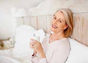 Portrait of a cheerful mature female holding coffee mug in bed